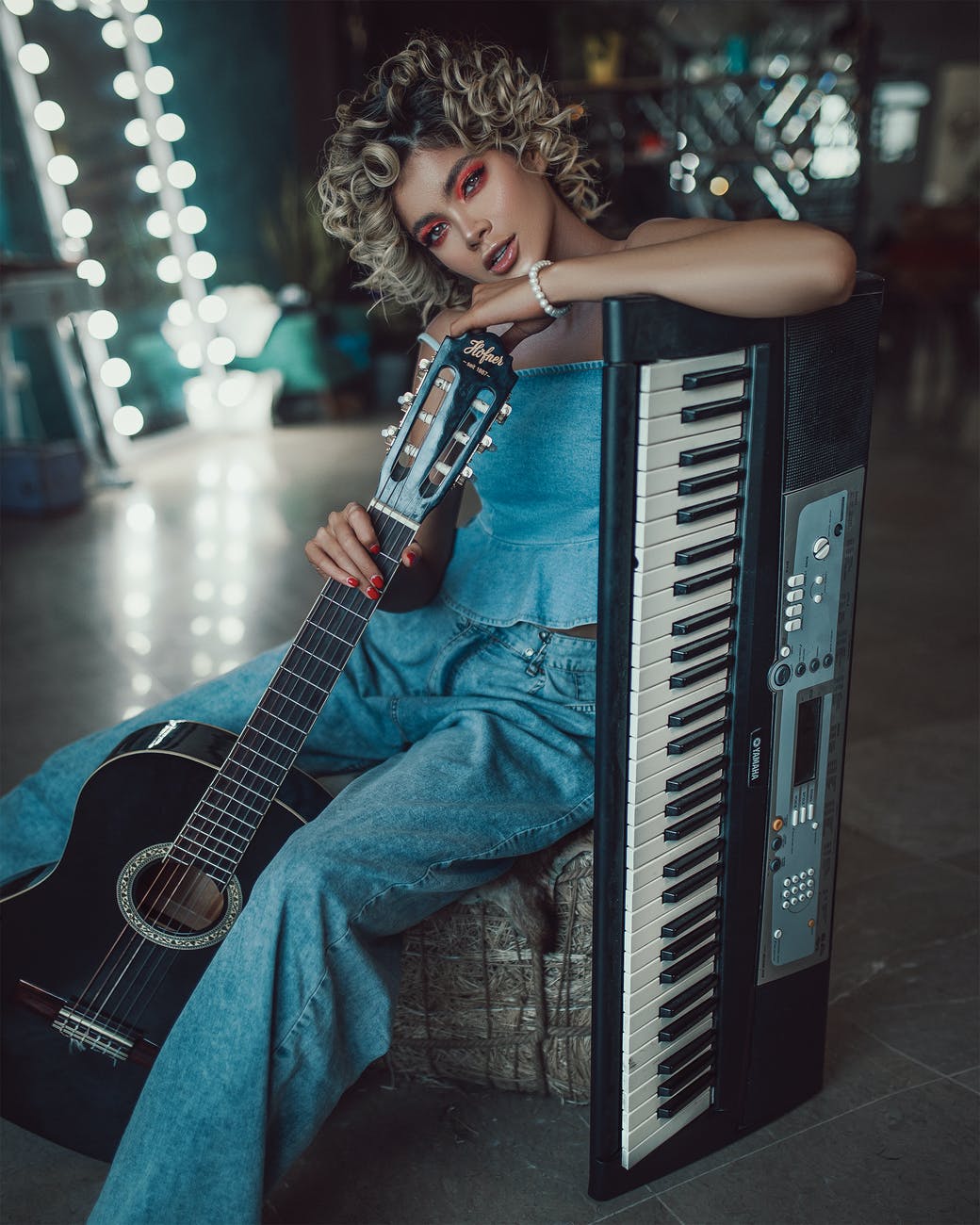trendy young female musician with guitar and synthesizer resting behind scene